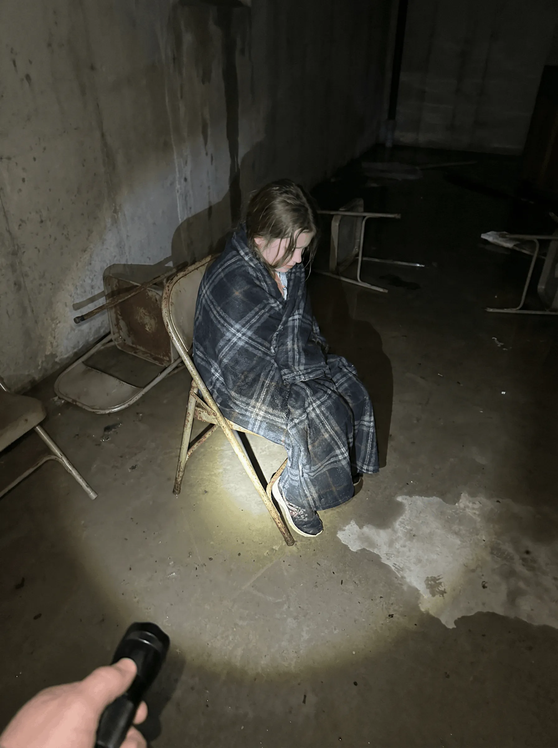 A young girl shivering under a thin blanket in a dark church basement during a power outage
