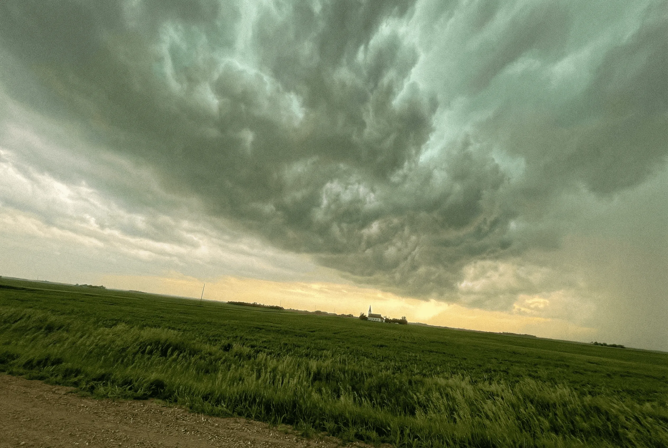 Ominous greenish storm clouds rolling over a rural field with a church steeple in the distance