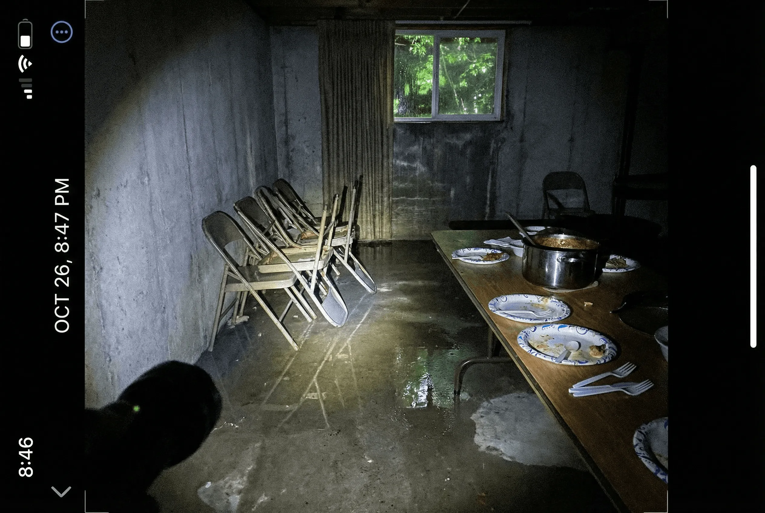 A dark church basement during a power outage with scattered chairs and water on the floor